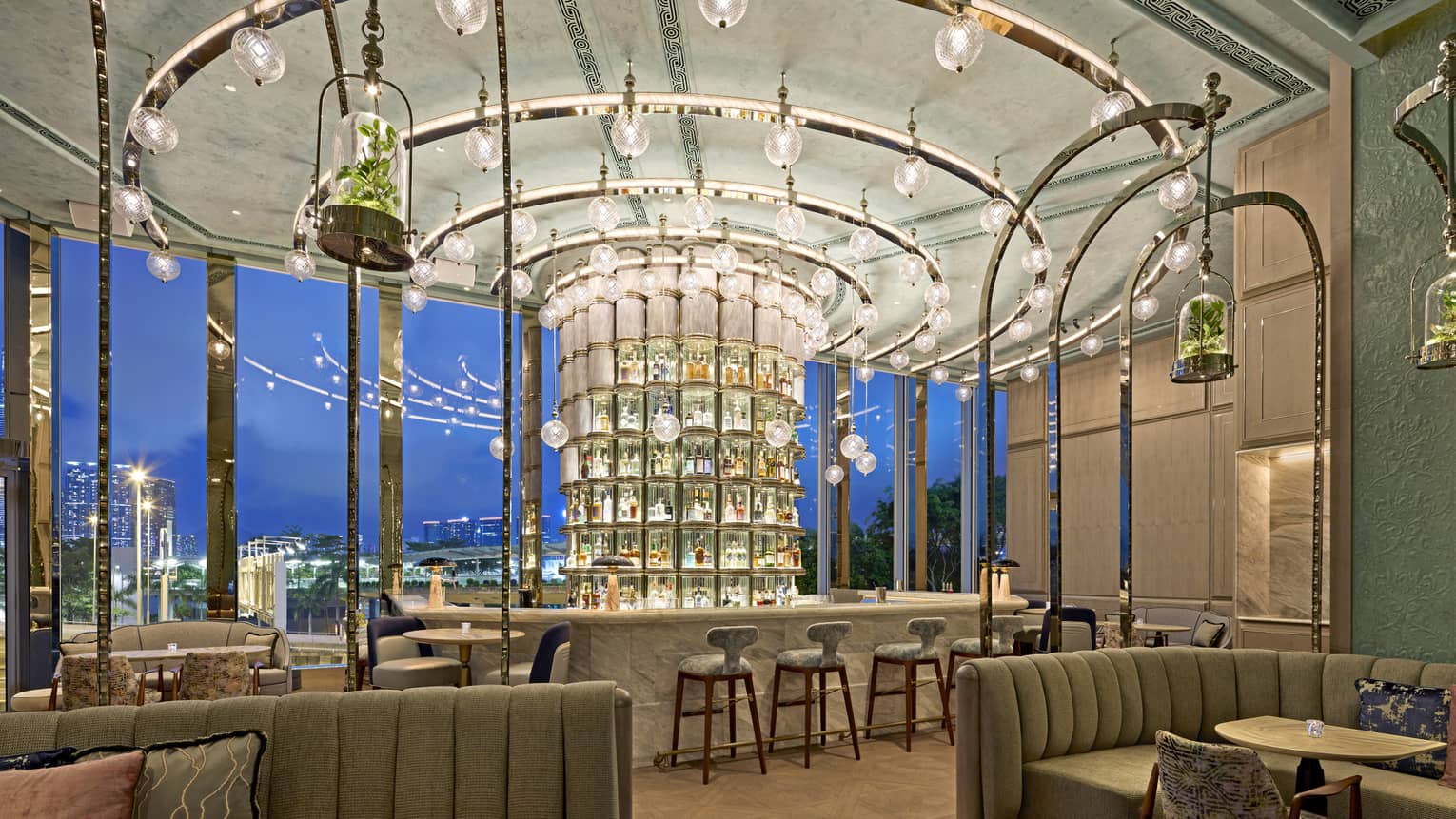Luxurious bar with a circular illuminated liquor display, hanging glass globes, arching metallic fixtures and large windows overlooking a cityscape.