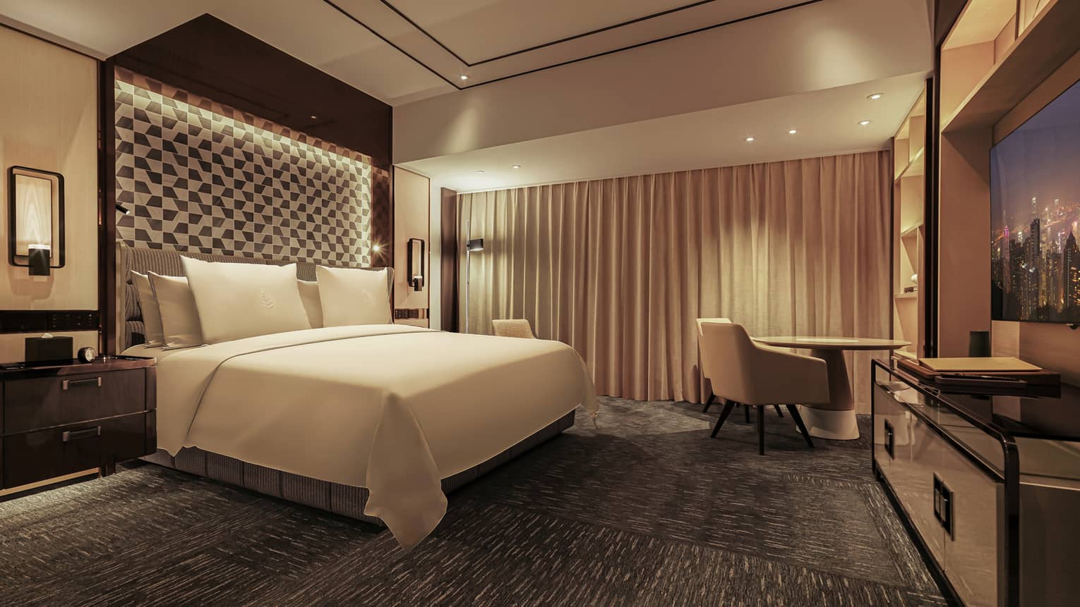 Luxurious hotel bedroom with king-size bed, geometric accent wall, warm lighting, beige curtains and small seating area with table and chair.