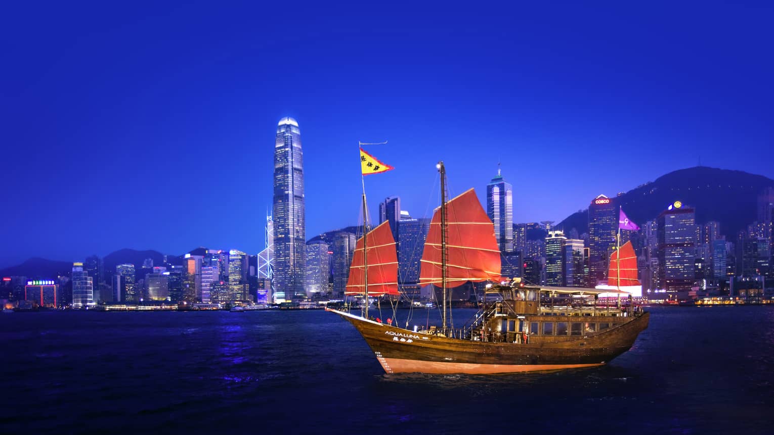 Ship with red sails cruises along the water with views of downtown in the background and clear blue sky