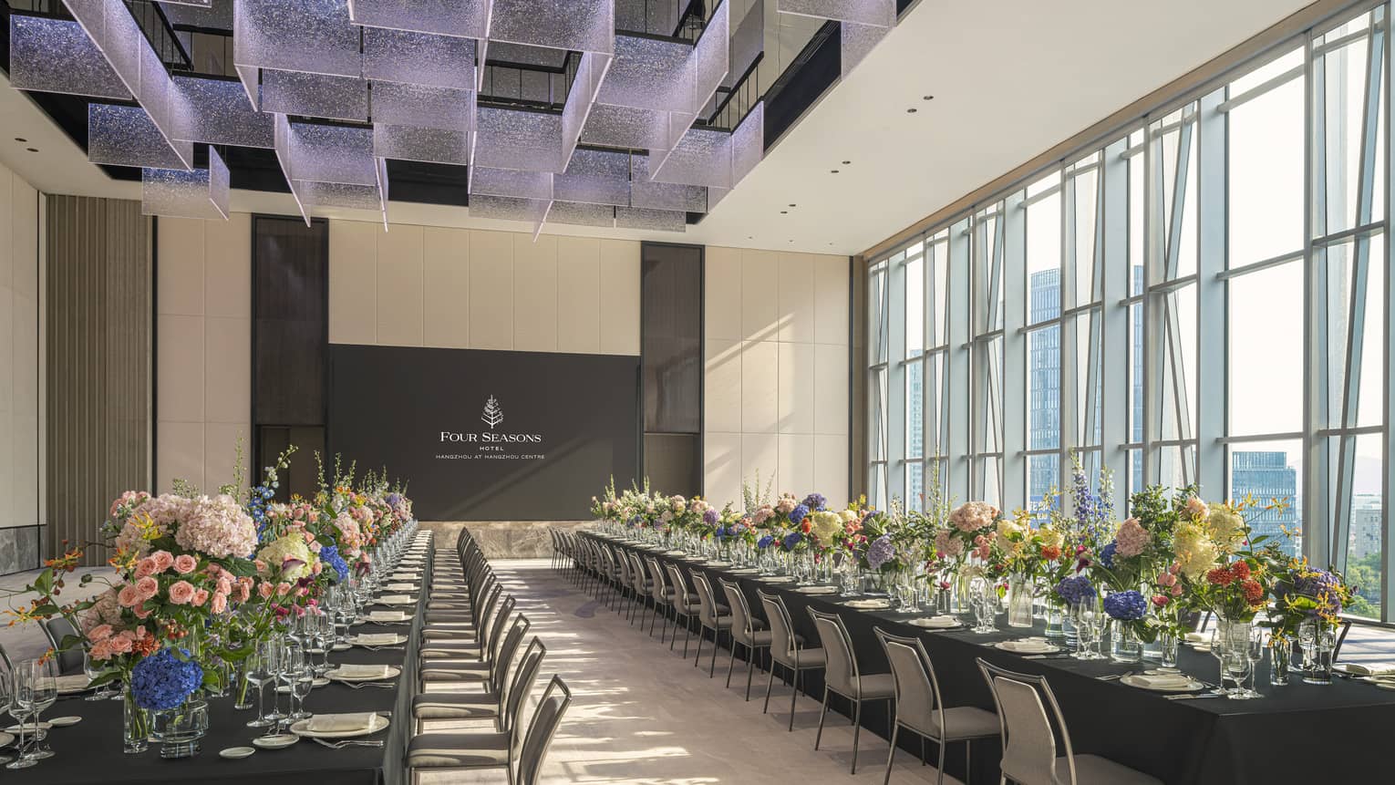Hotel ballroom featuring two extra-long tables, each lined with floral arrangements and place settings