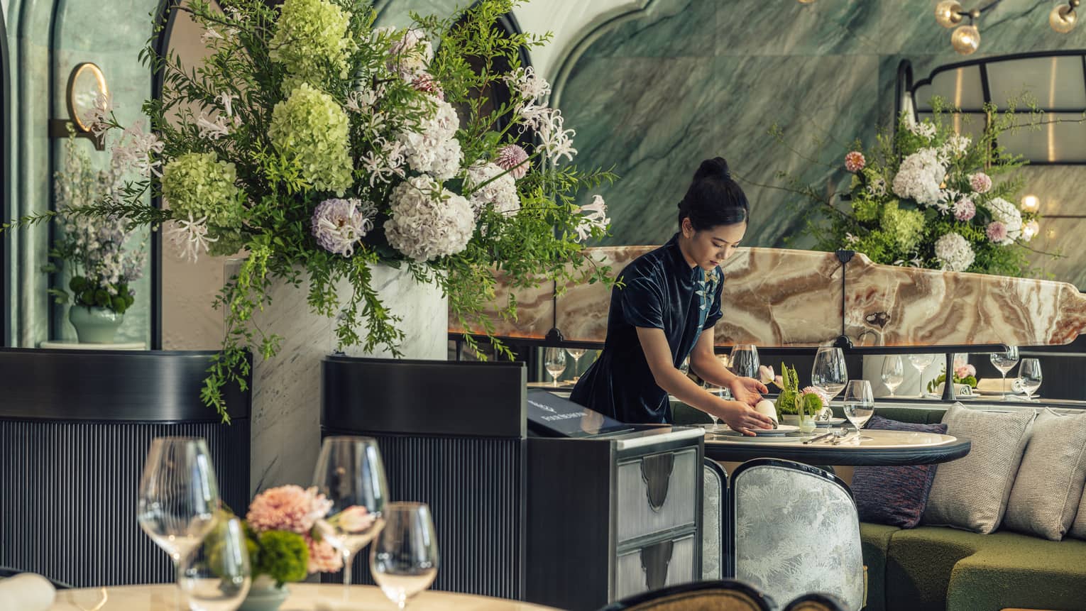 Woman sets table next to large floral arrangement at Chinese restaurant Song at Four Seasons Hotel Hangzhou at Hangzhou Centre