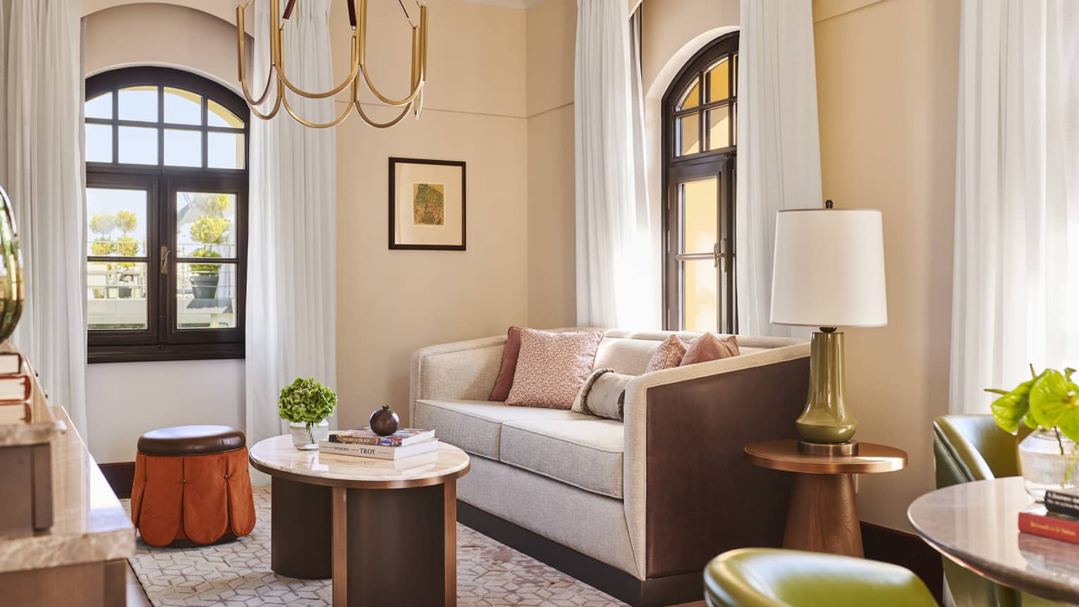 Living room with light pink walls, grey sofa, two arched windows, chandelier, coffee table