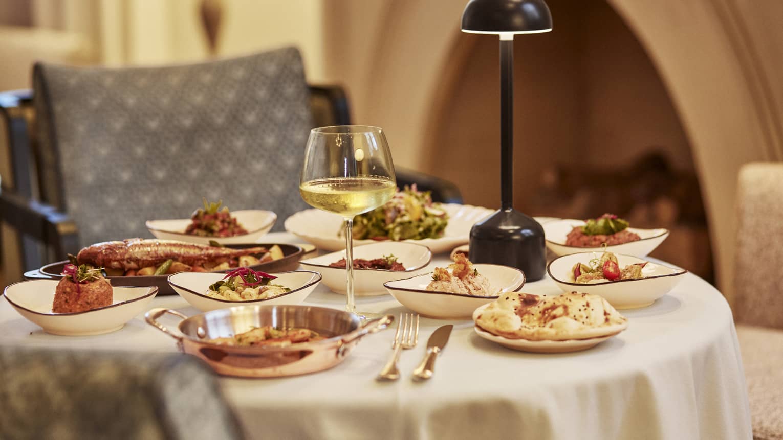 Round table set with multiple mezze plates and glass of white wine