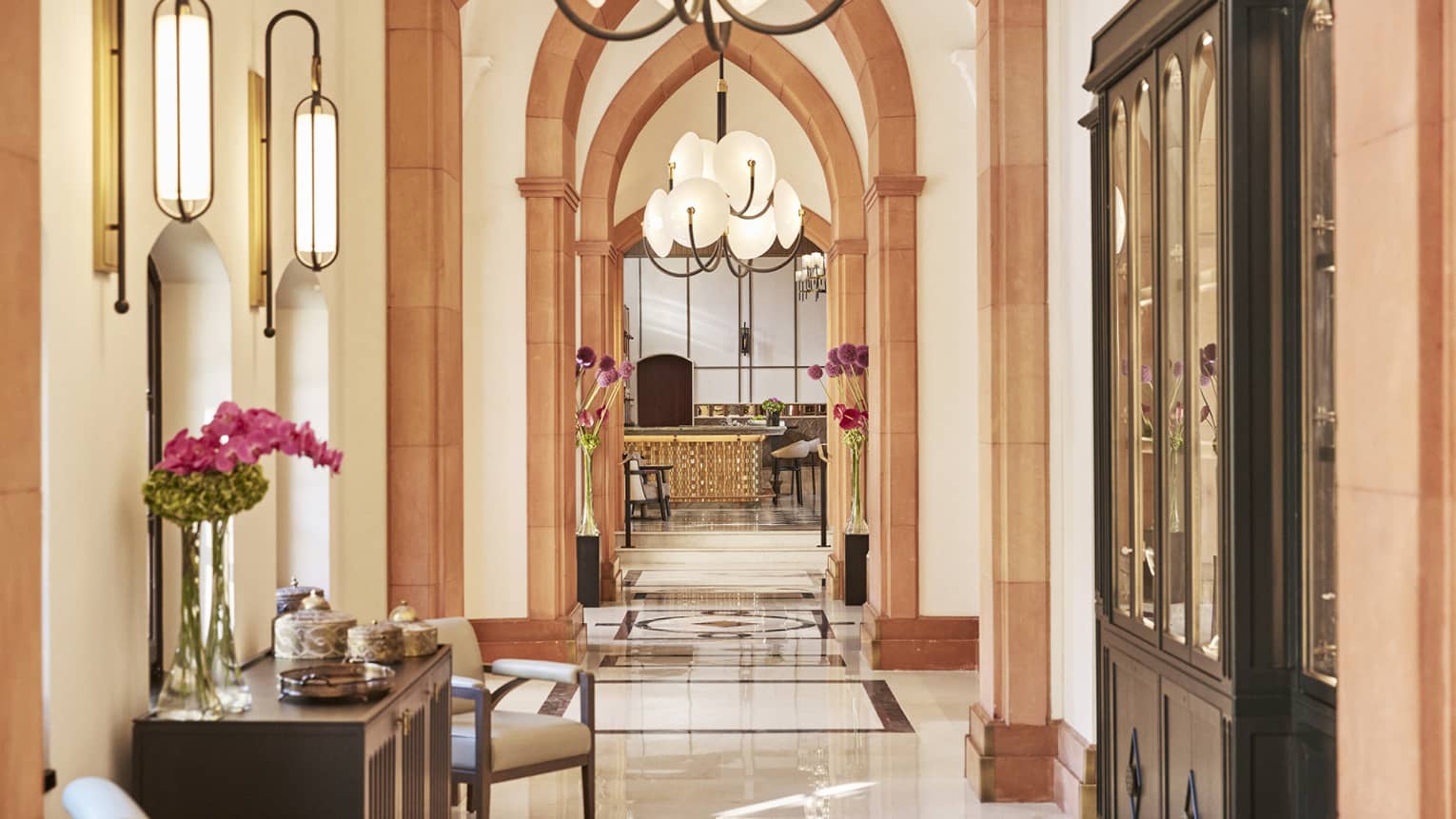 A long hall with arches, a counter with flowers and chairs to sit on.
