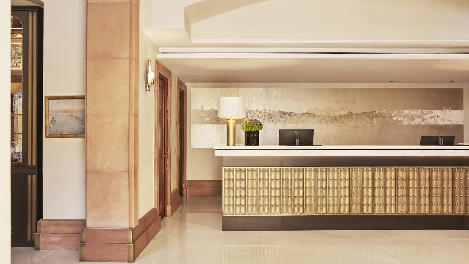 The lobby of a hotel with beige colouring and a large counter with computer screens.