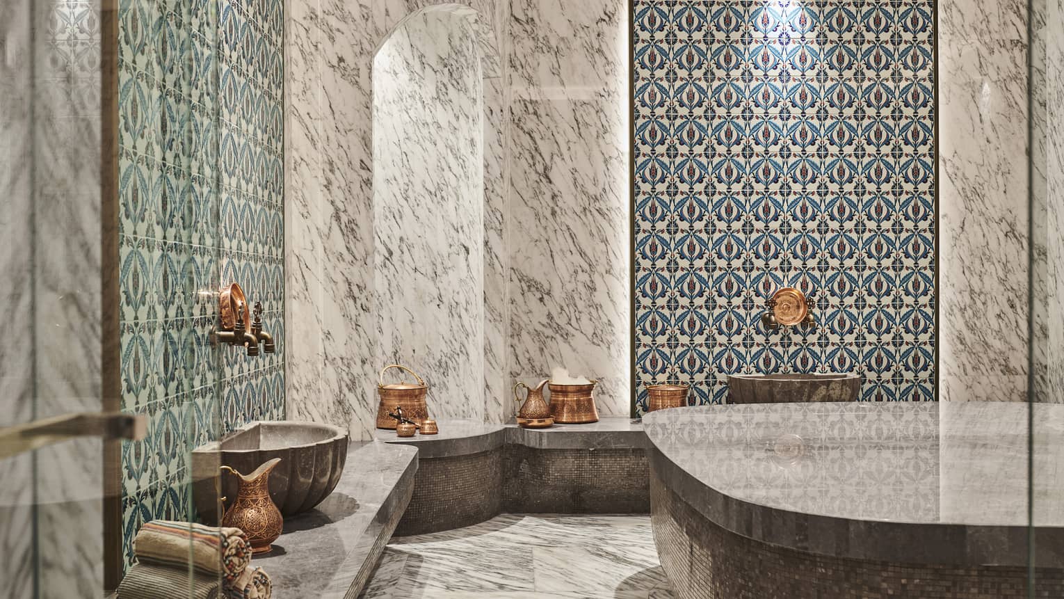 Steam shower with mosaic tile and full marble walls, floor and benches, and brass urns