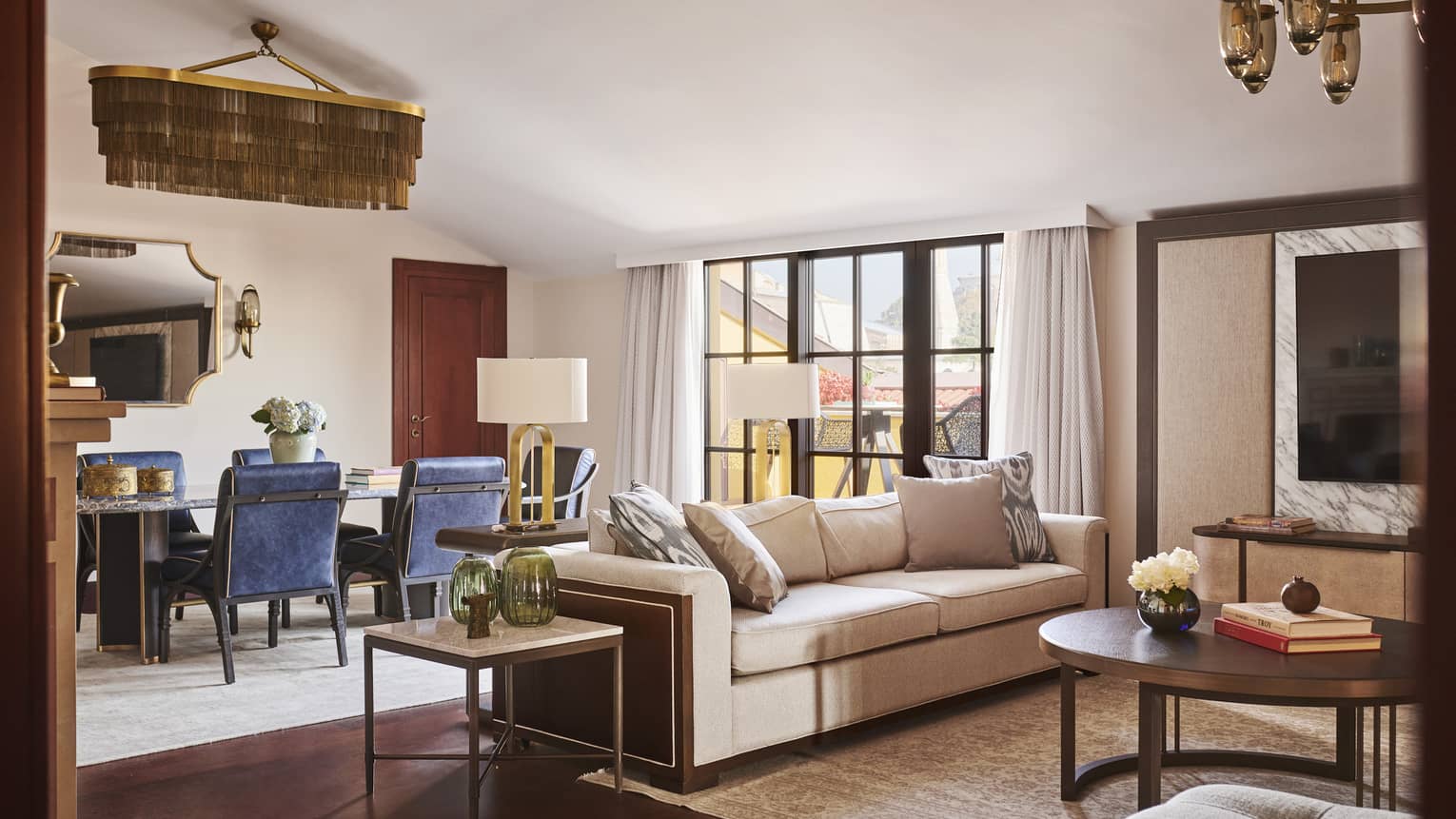 Hotel suite contemporary dining room with blue chairs beside neutral living area with couch, round coffee table and beige ottoman