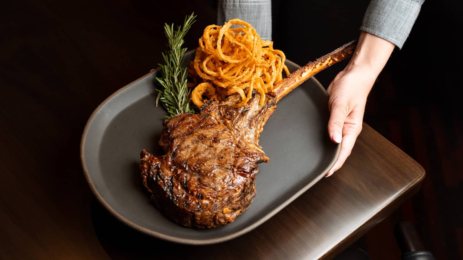 A person serving a large steak and onion rings on a plate