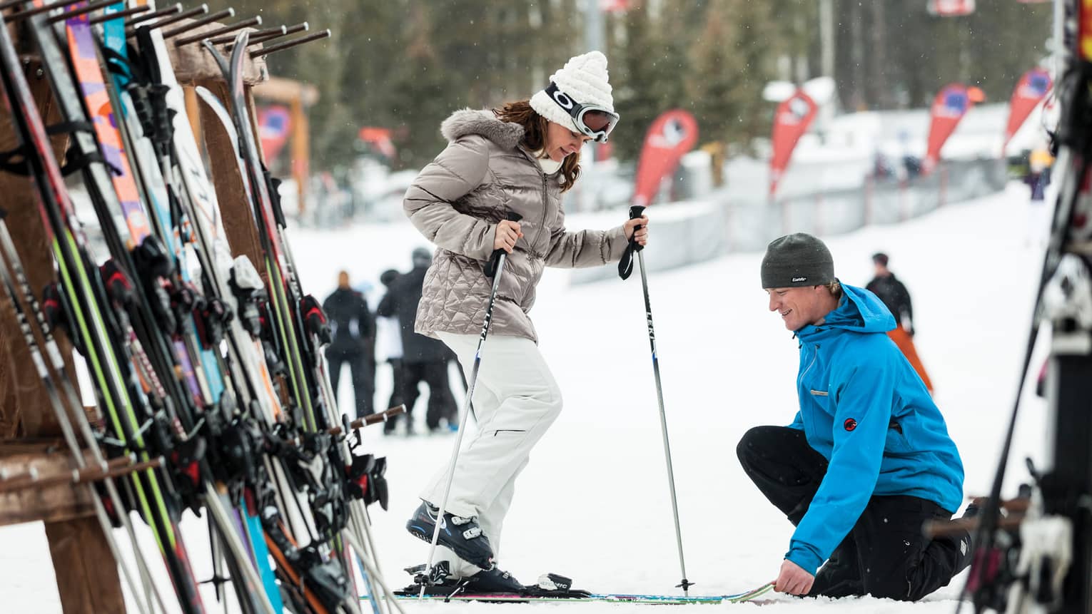 Hotel staff holds skis as woman holding poles steps in by ski rack, snowy hill
