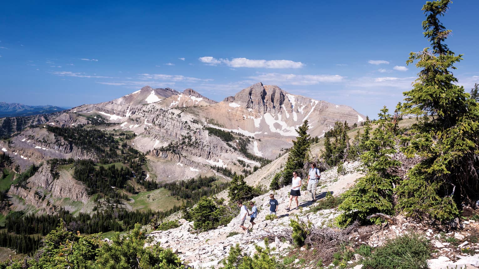 Family hikes along rocky path on mountain, sweeping views of mountain range