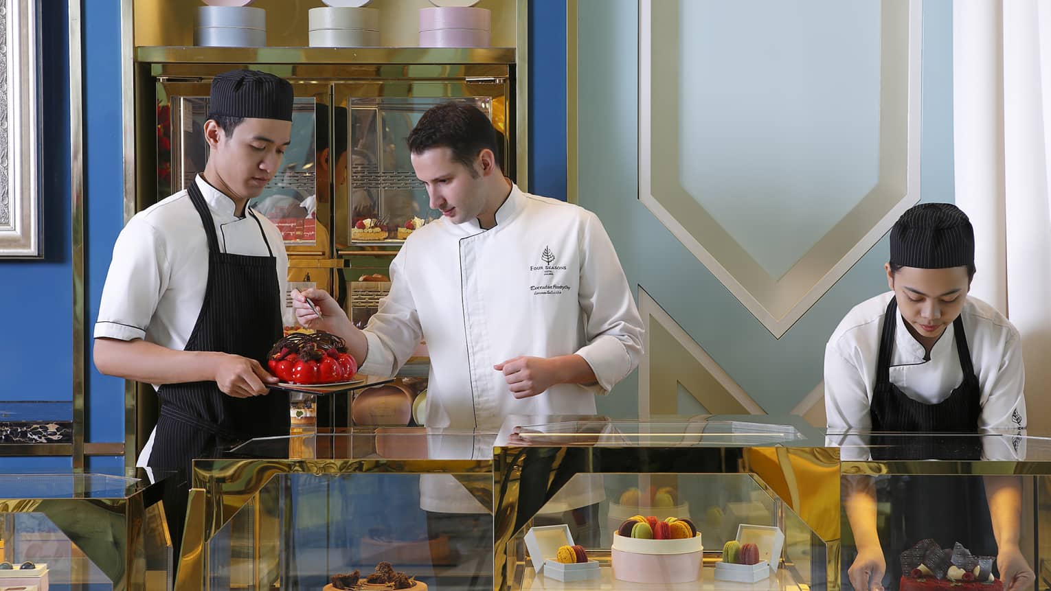 Three chefs with cakes, desserts at pastry counter 
