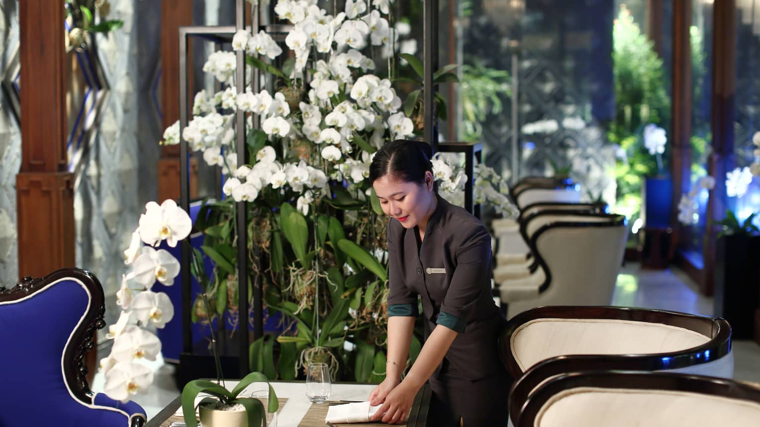 Hotel staff sets dining table near tall white orchids 