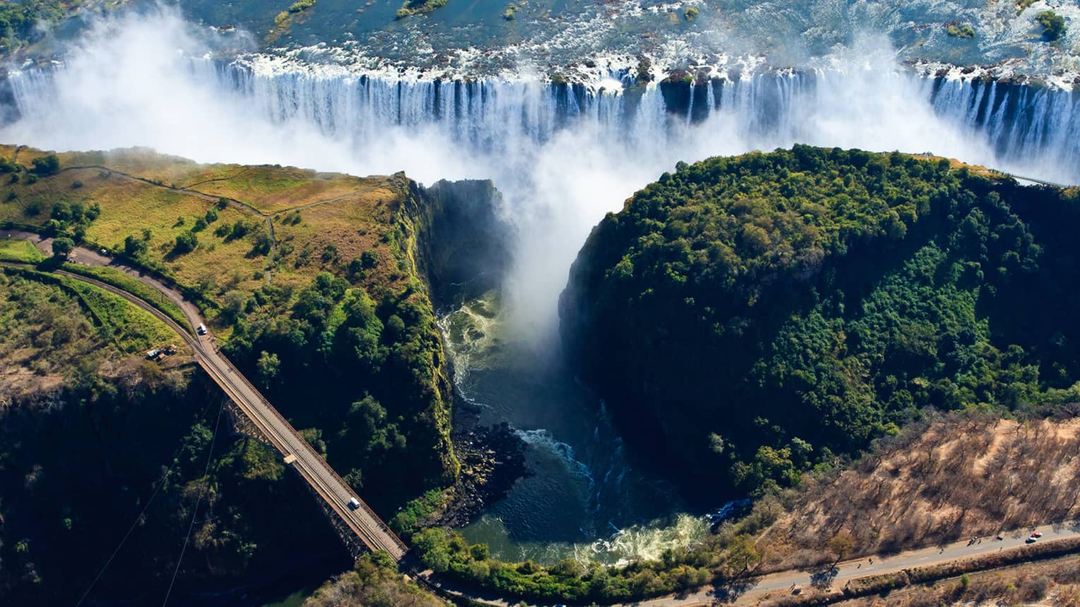 An aerial view of Victoria Falls with a long winding road running across the landscape