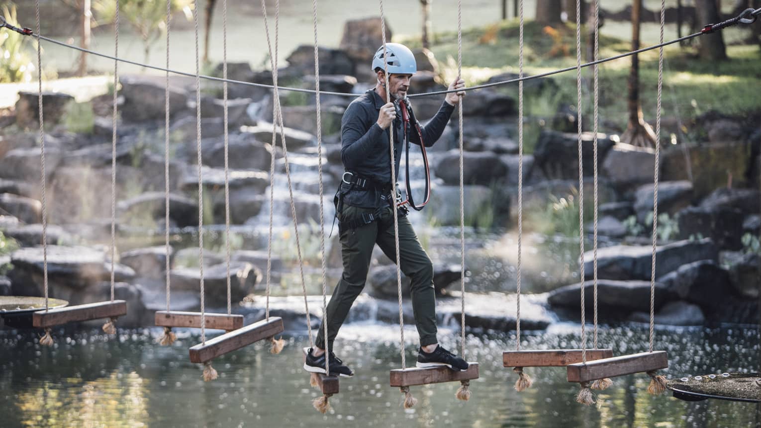 A man walks across hanging wooden blocks at ropes course
