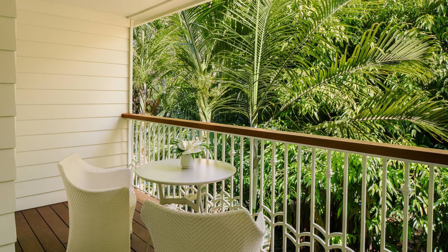Private lanai of a resort room with two chairs and small round table, looking out to tropical palm trees