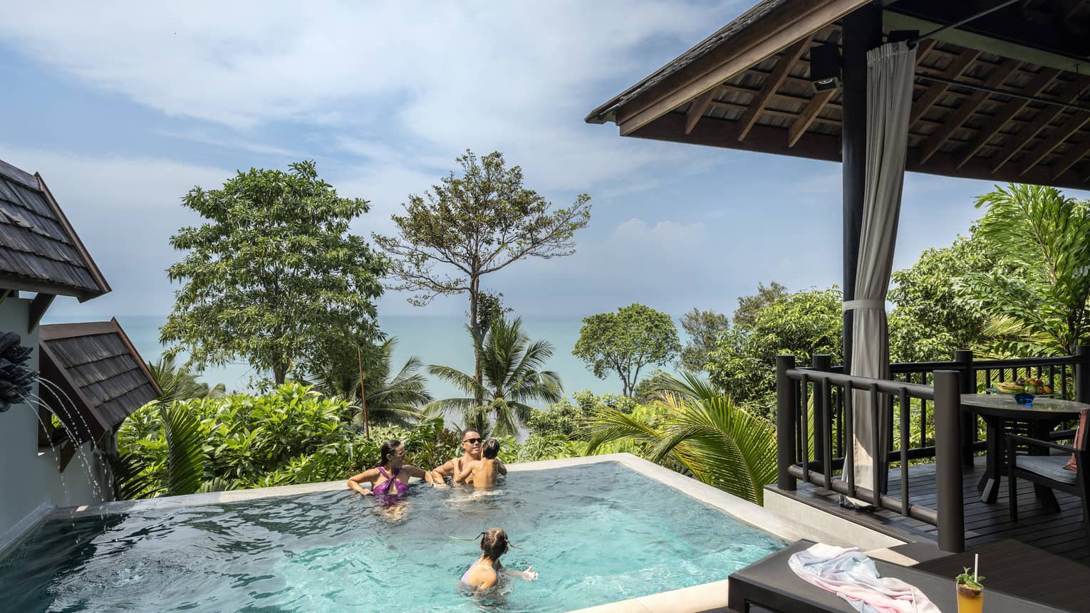 Man, woman and young boy swim in small pool overlooking trees and the sea