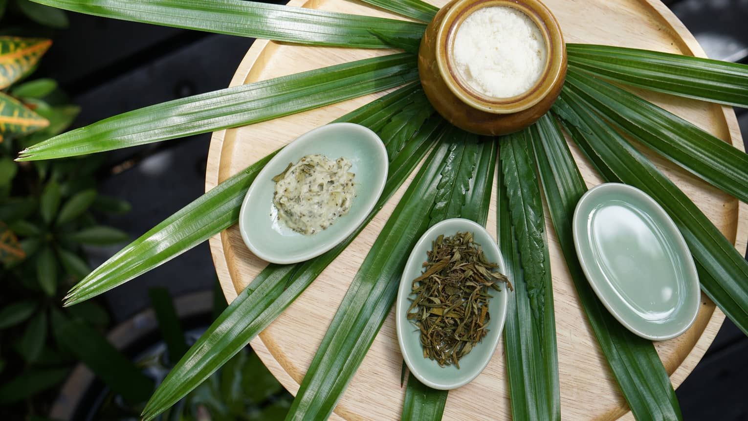 Pandan leaves laid out like a fan on a wooden table with a jar and small bowls of herbs and scrubs placed on top.