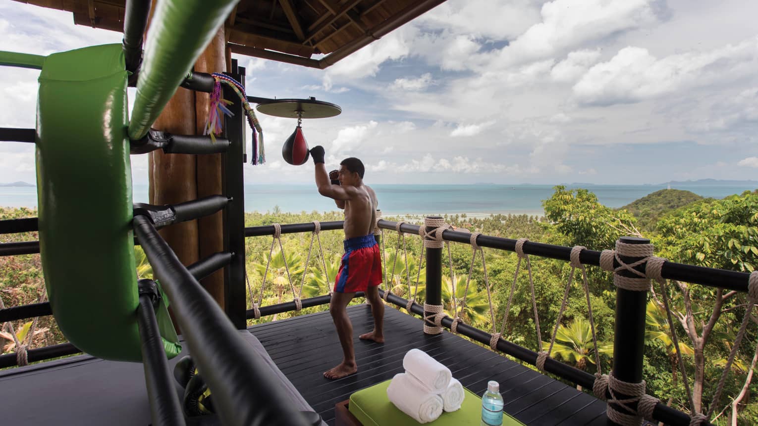 Muay Thai boxer hitting bags on wood deck high up on mountain