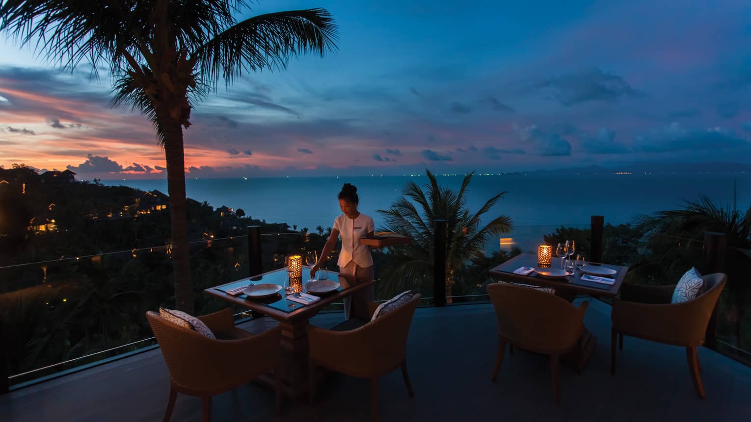 Waitstaff sets the table on outdoor terrace at Koh Thai Kitchen in Koh Samui, view of palm trees and Gulf of Thailand