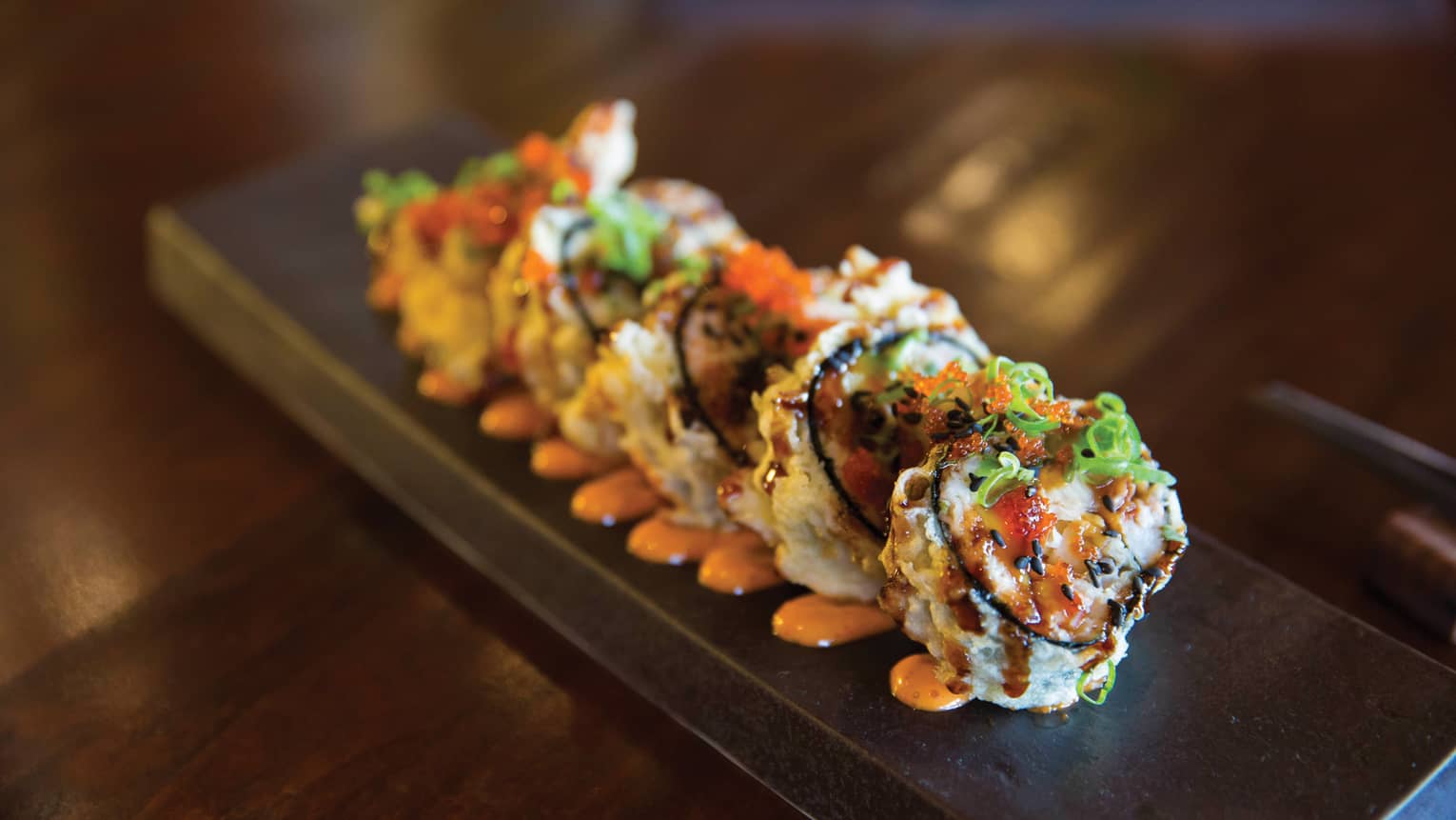 Crunchy shrimp sushi rolls arranged on long tray, orange sauce