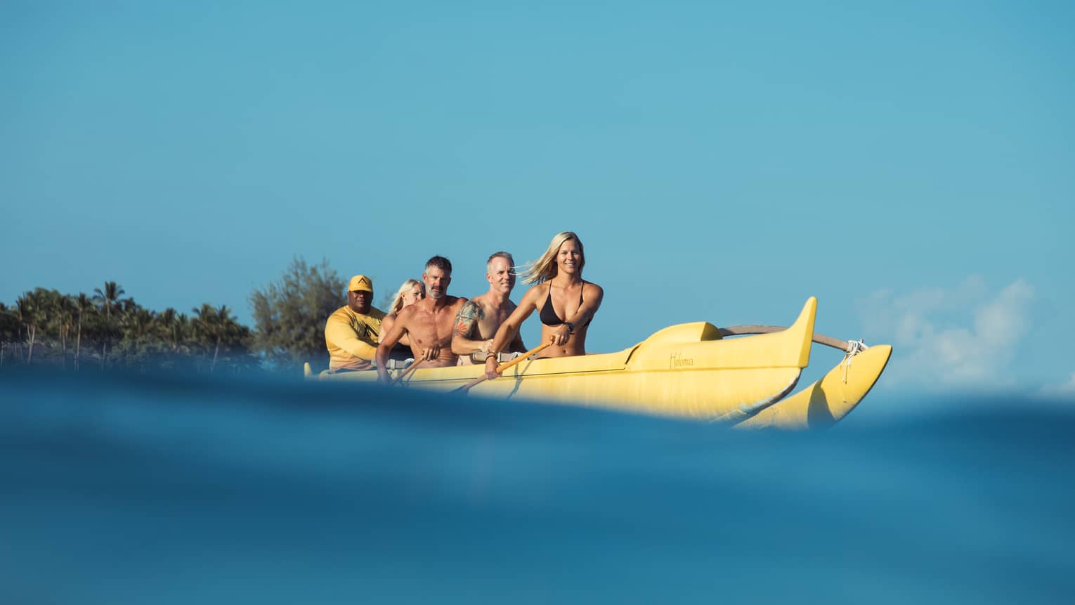Group of friends with paddles row in large yellow canoe, Four Seasons resort staff at back