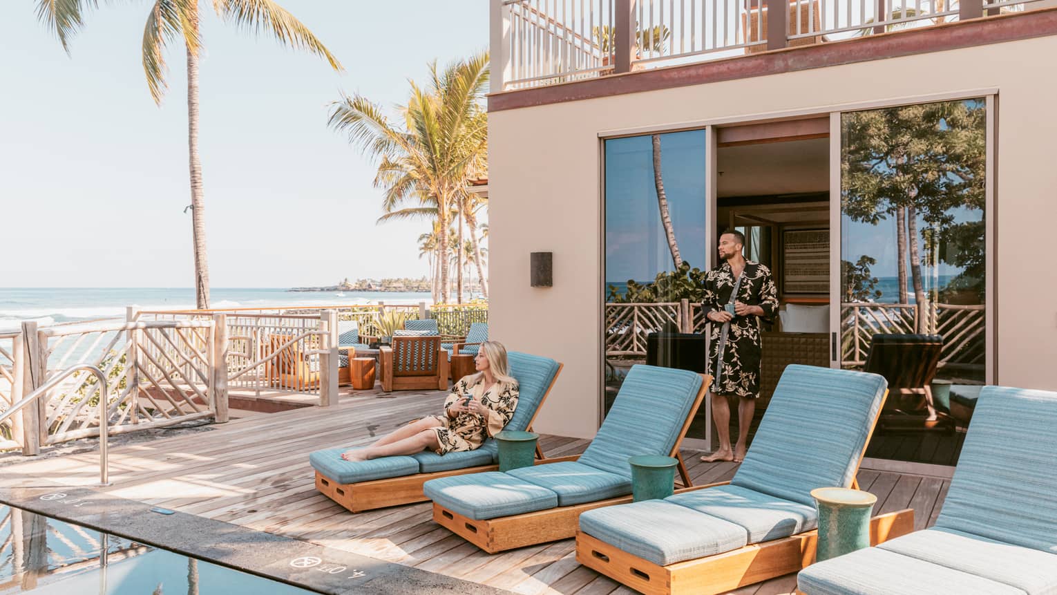 Private pool terrace, woman sits on one of four sun loungers with turquoise cushions