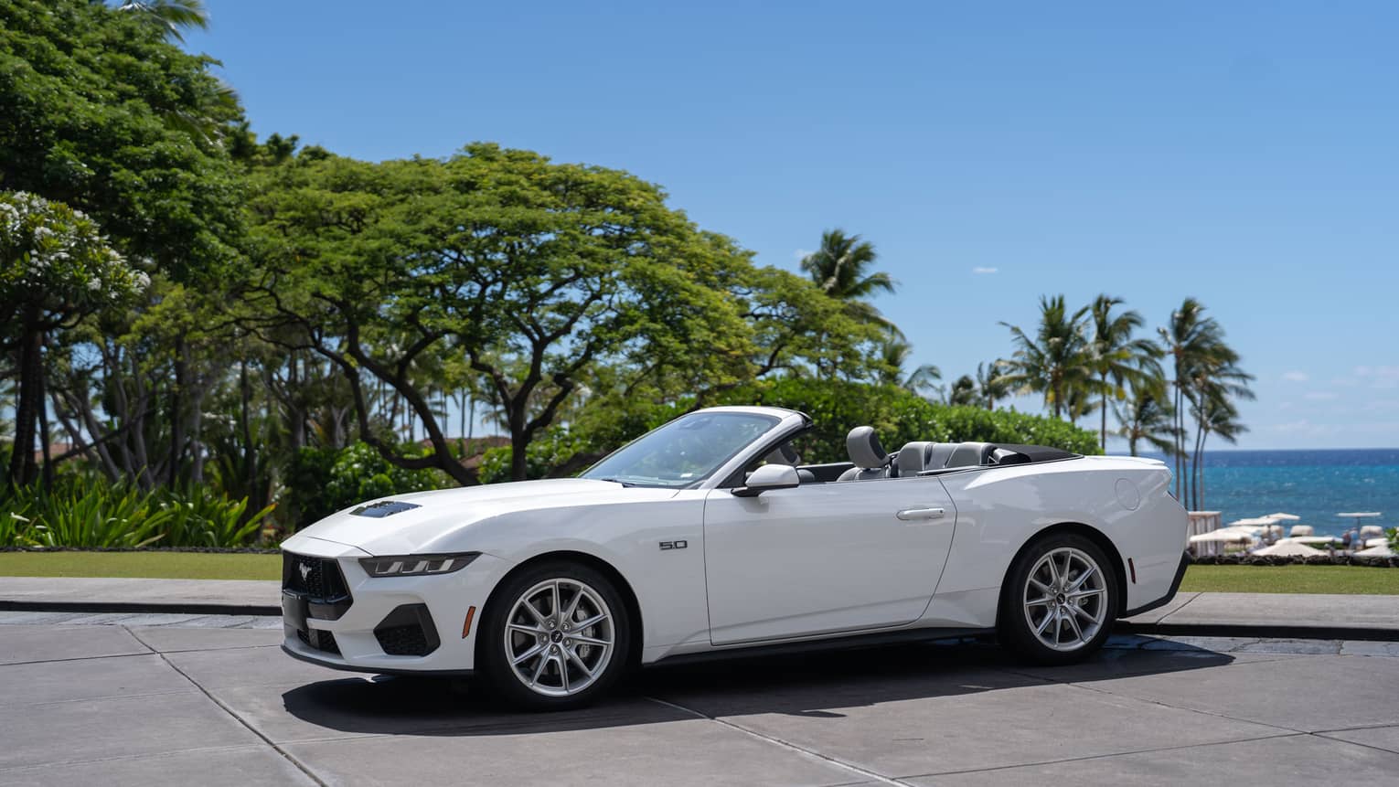 White convertible car parked in front of tropical beach setting