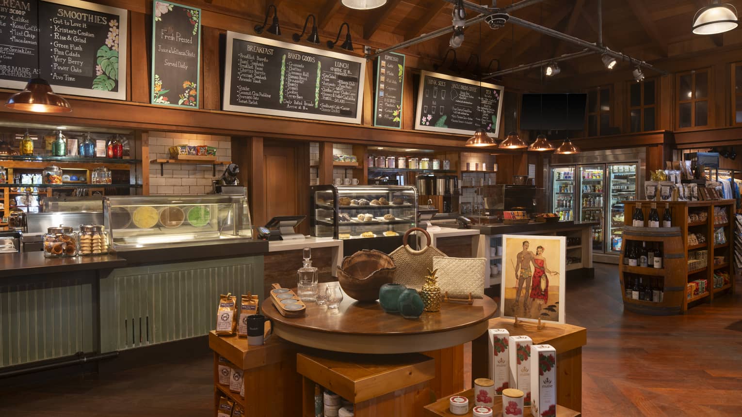 A spacious, well-lit area with warm wood decor, a counter with menus overhead and display cases of food items. There are also stocked shelves and free-standing displays of items in the space.