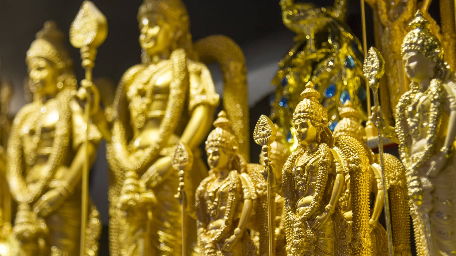 Side view of rows of golden statues in various sizes, each holding a tall spear and donning an ornate headdress and attire.