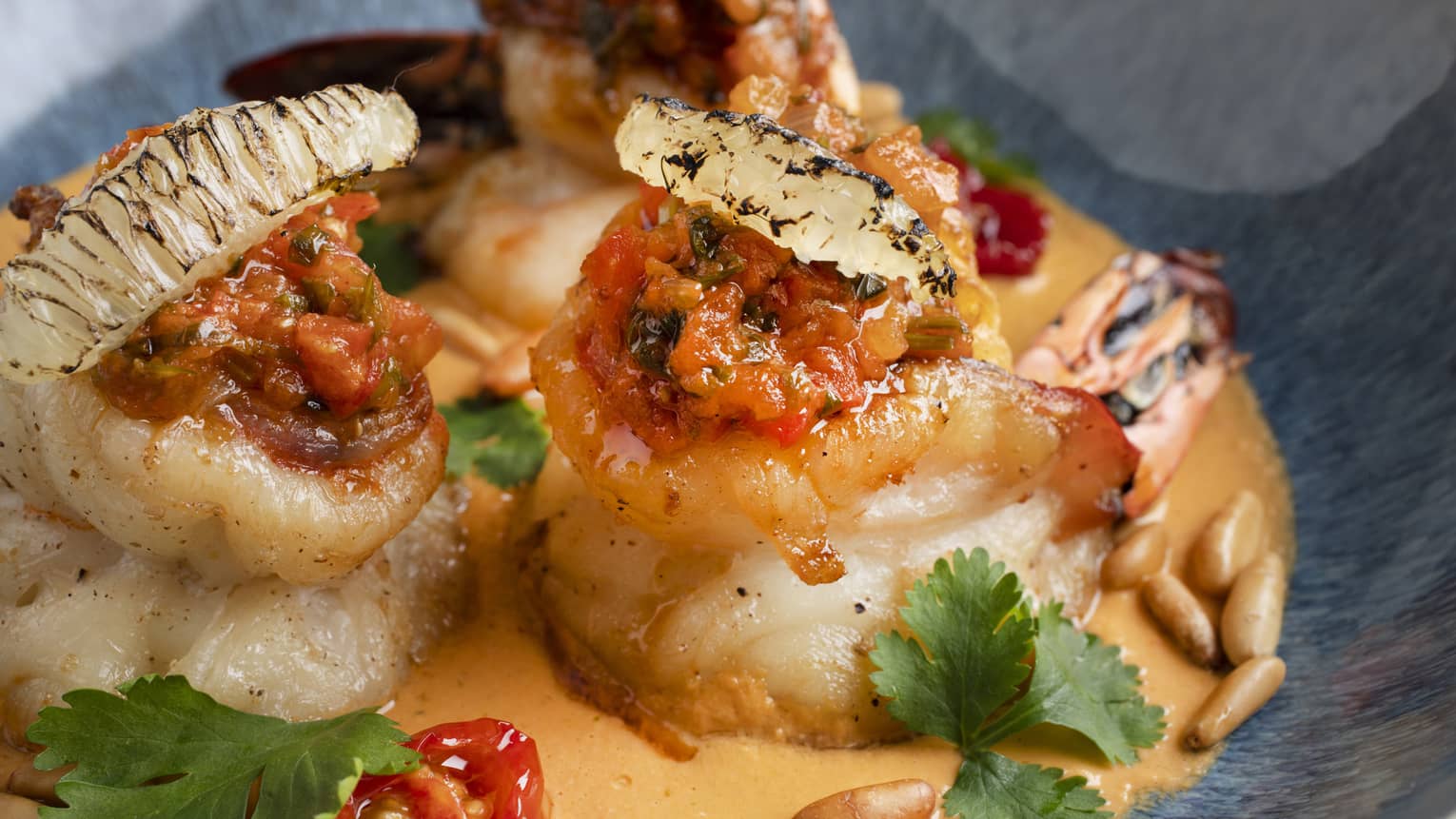 Grilled shrimp served with shakshouka sauce, peanuts and parsley as garnish in a light-blue bowl