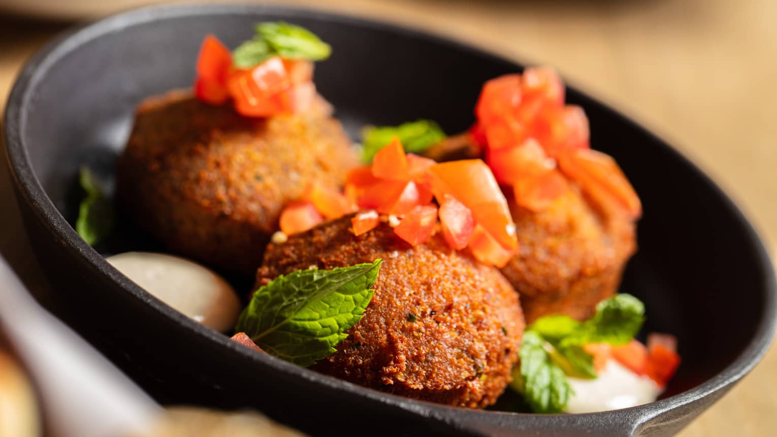 Falafel in a skillet topped with tomatoes and mint.