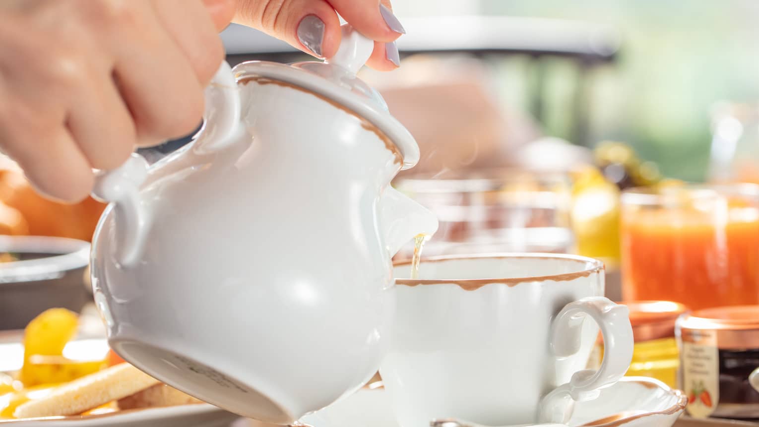 A woman pours a glass of tea using a white porcelain tea set
