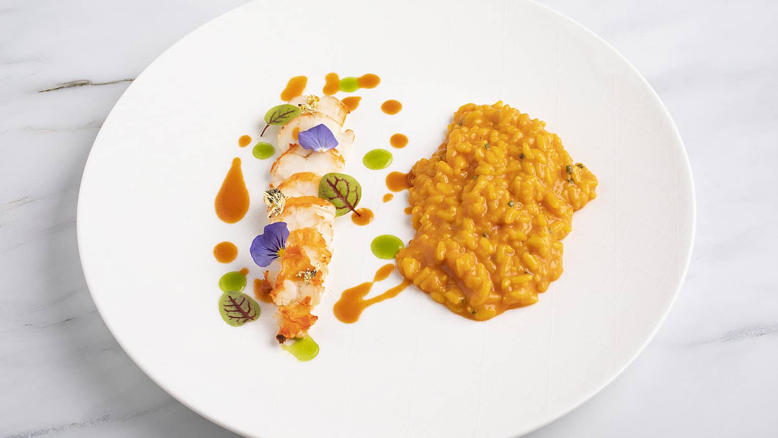 Risotto topped with red and green sauce, and served beside filet-of-fish, all served on a white porcelain plate.