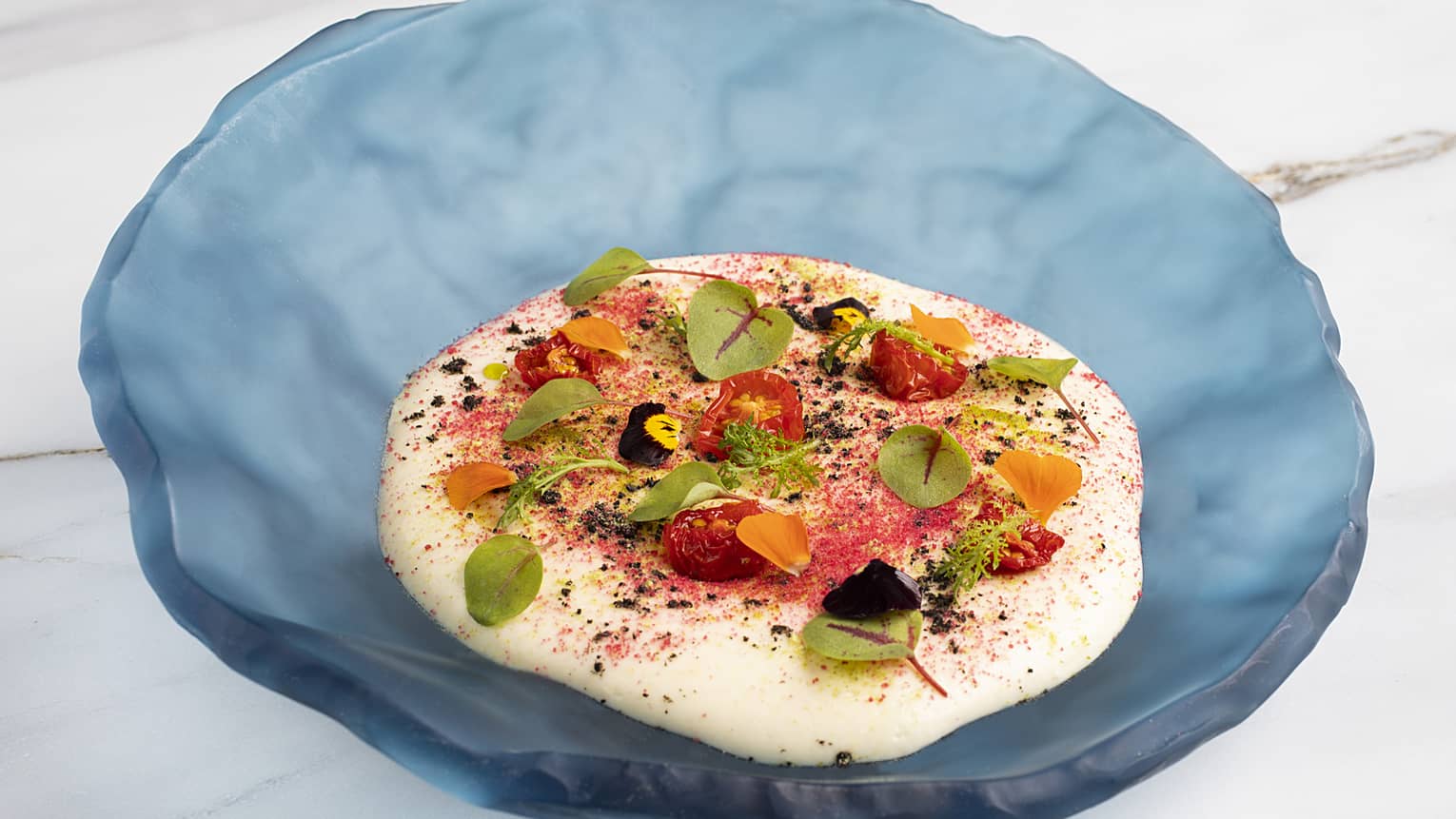Potato foam topped with octopus, tomatoes and various greenery served in a blue platter.