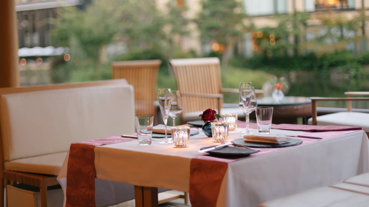 Elegant outdoor dining table set with wine glasses, a small red rose centerpiece and soft lighting at Four Seasons 