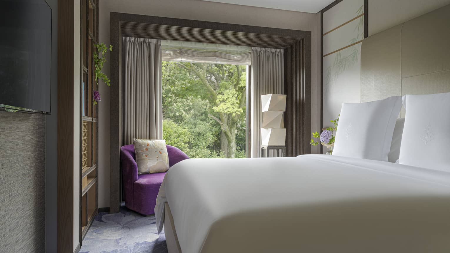 Spacious hotel bedroom with a king-size bed, purple armchair and floor-to-ceiling windows overlooking the garden
