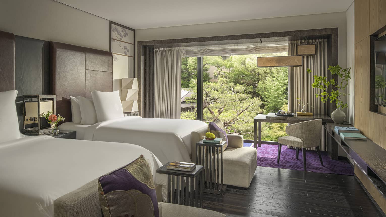 Guest room with two beds, a writing desk and a large window overlooking a lush pond garden 