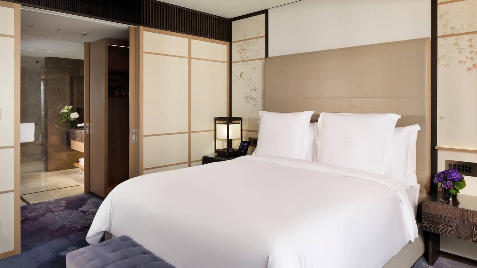 Elegant bedroom with a king-size bed, soft accent lighting, and sliding doors leading to a spacious bathroom at Four Seasons
