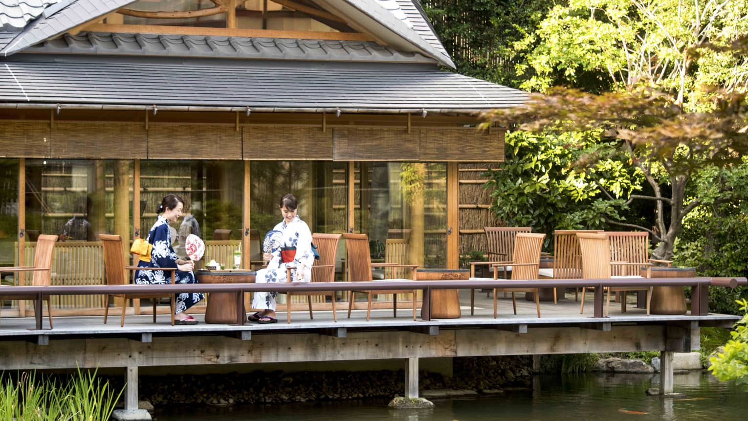 Two women in traditional Japanese garb observing the koi fish swimming below