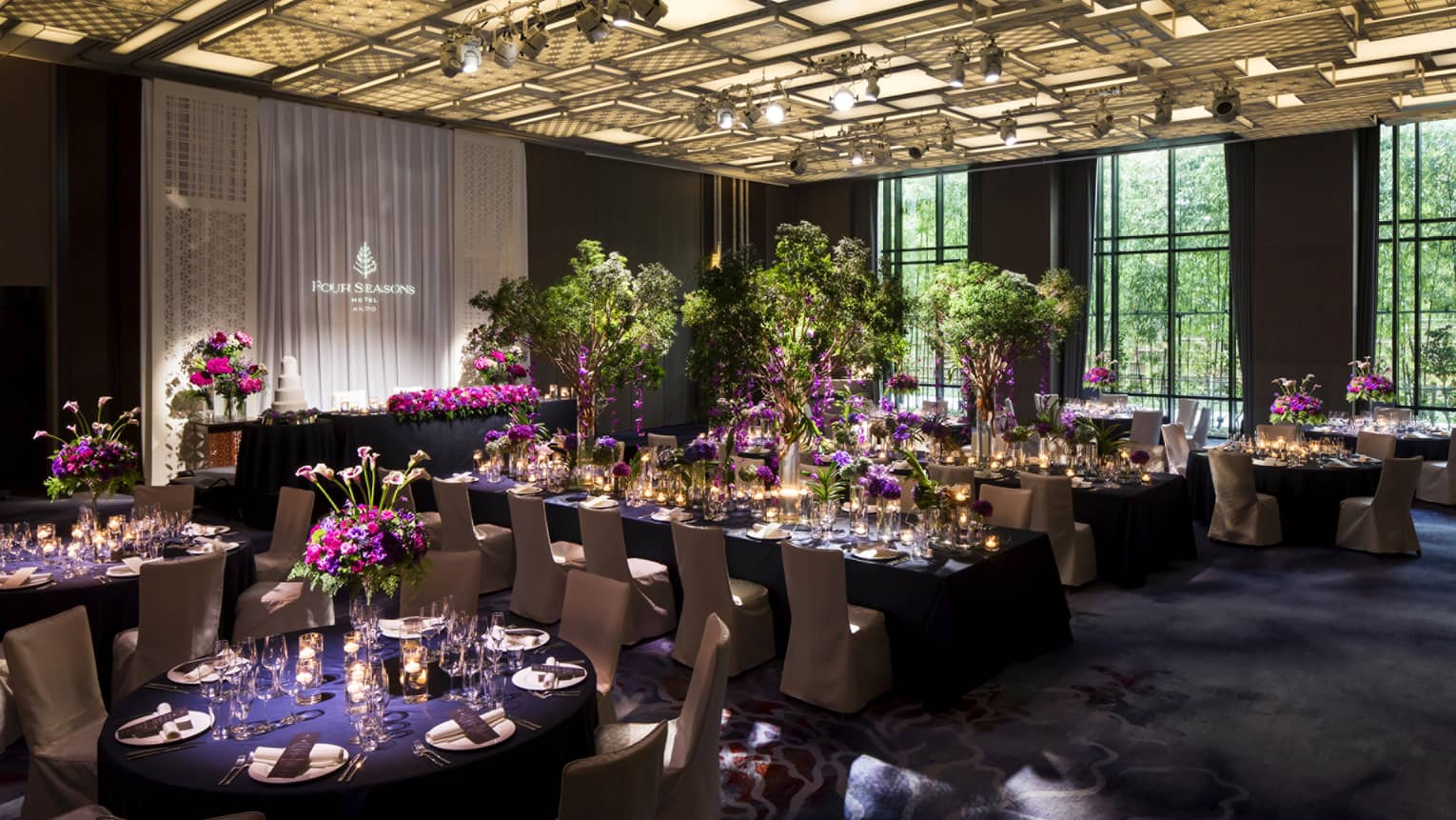 Elegant banquet hall at Four Seasons Hotel Kyoto with long tables set for a wedding reception, adorned with purple flowers and greenery.