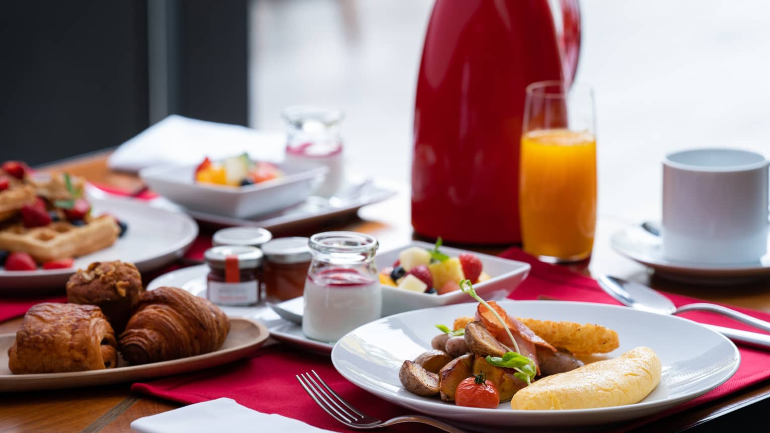 Breakfast foods (waffles, pastries, omelette with potatoes, fruit, etc.), orange juice and coffee on a table