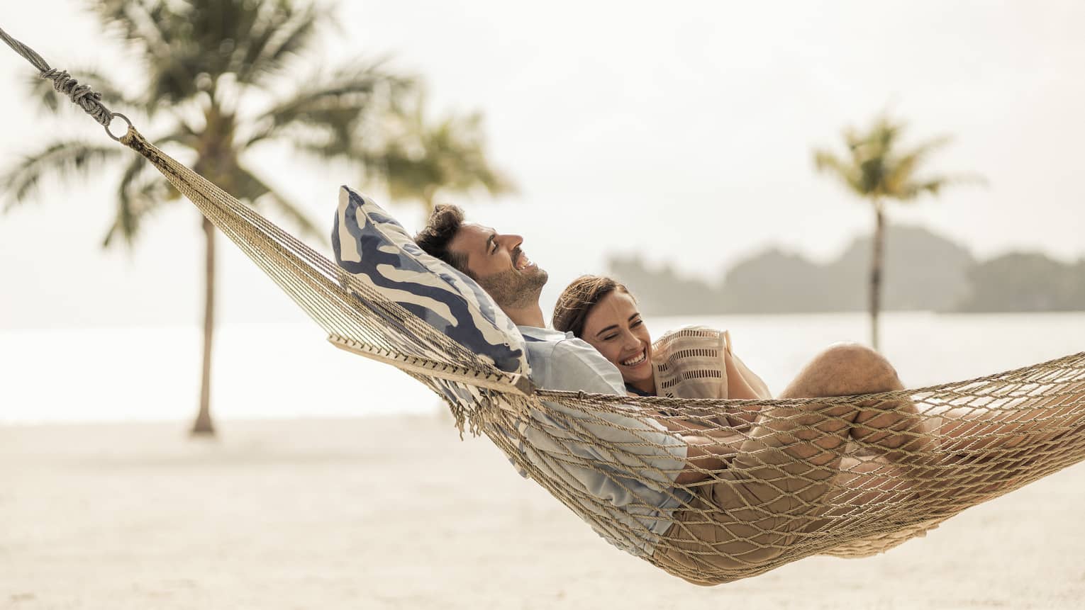 Couple lounges in hammock on sand beach