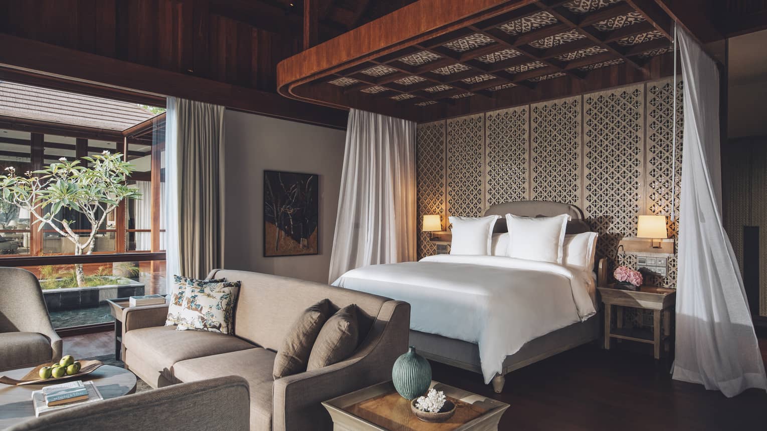 Bedroom with intricate ceiling design above white king bed, plus sofa and two arm chairs