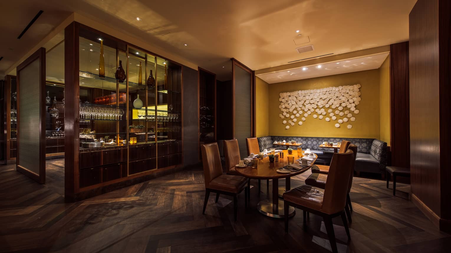 Culina Restaurant dining table, large booth in dimly-lit alcove by shelf display with wine glasses, vases