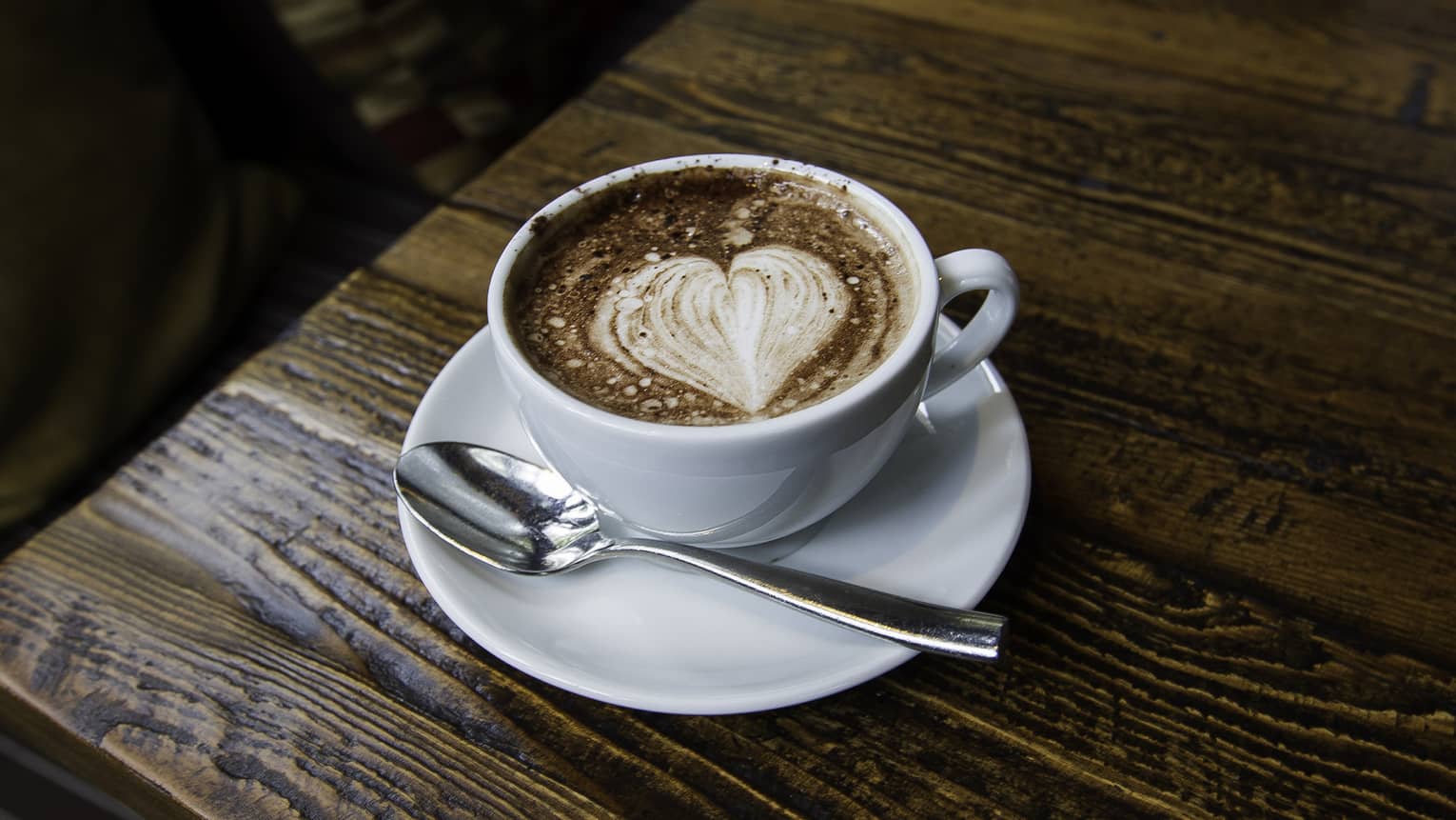 Creamy coffee with heart design in foam, white cup on wood table