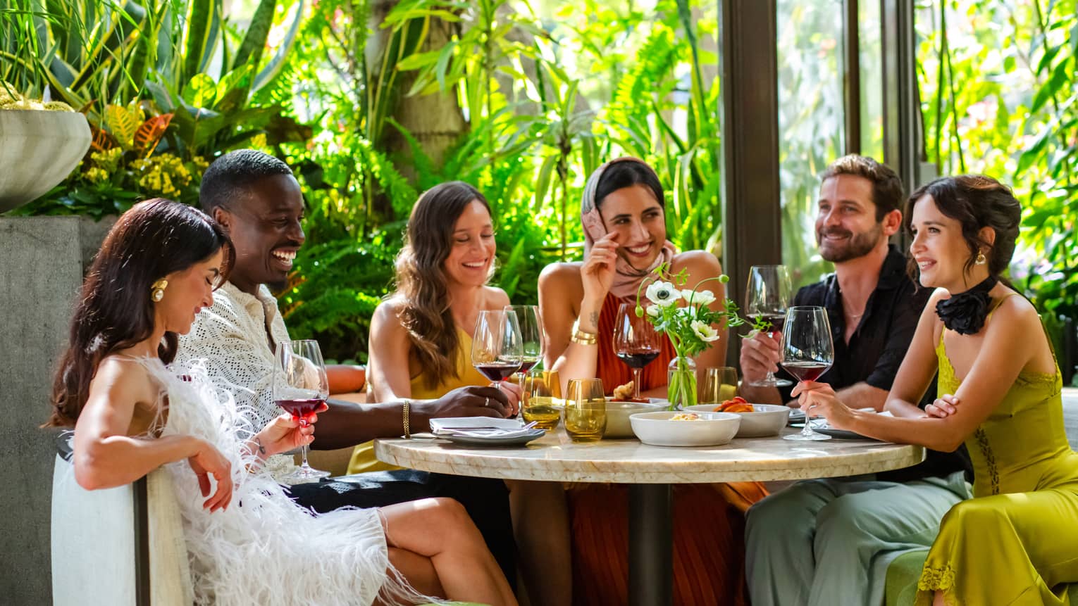 Group of friends dine together at round table at luxury hotel restaurant with greenery