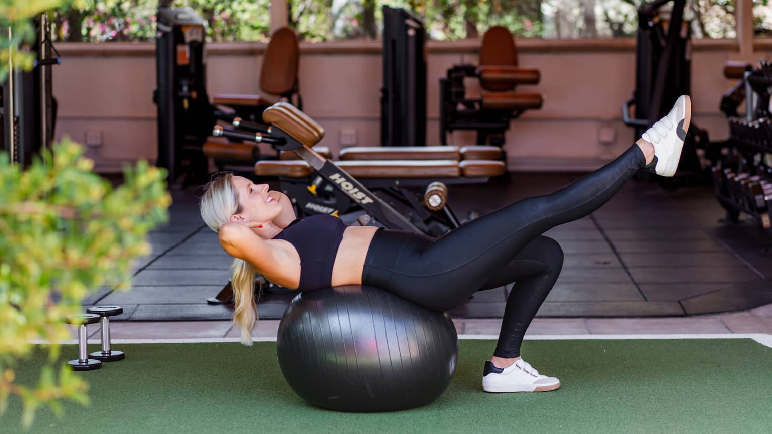 Woman does an exercise on a large exercise ball at indoor-outdoor luxury hotel gym