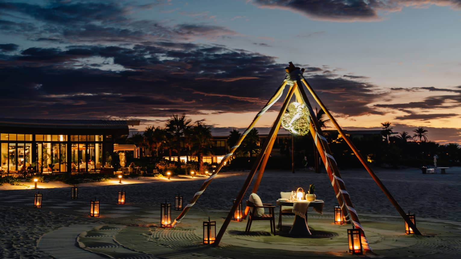 Outdoor tent with a chair and dining table, surrounded by lanterns on the ground in the evening.