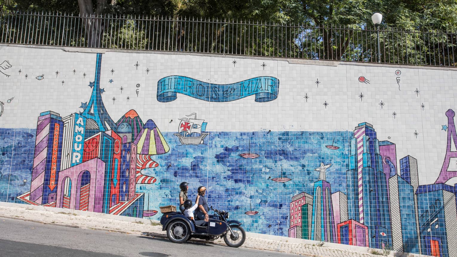 Two adults and a child stop their motorcycle to look at a city mural made of tiles