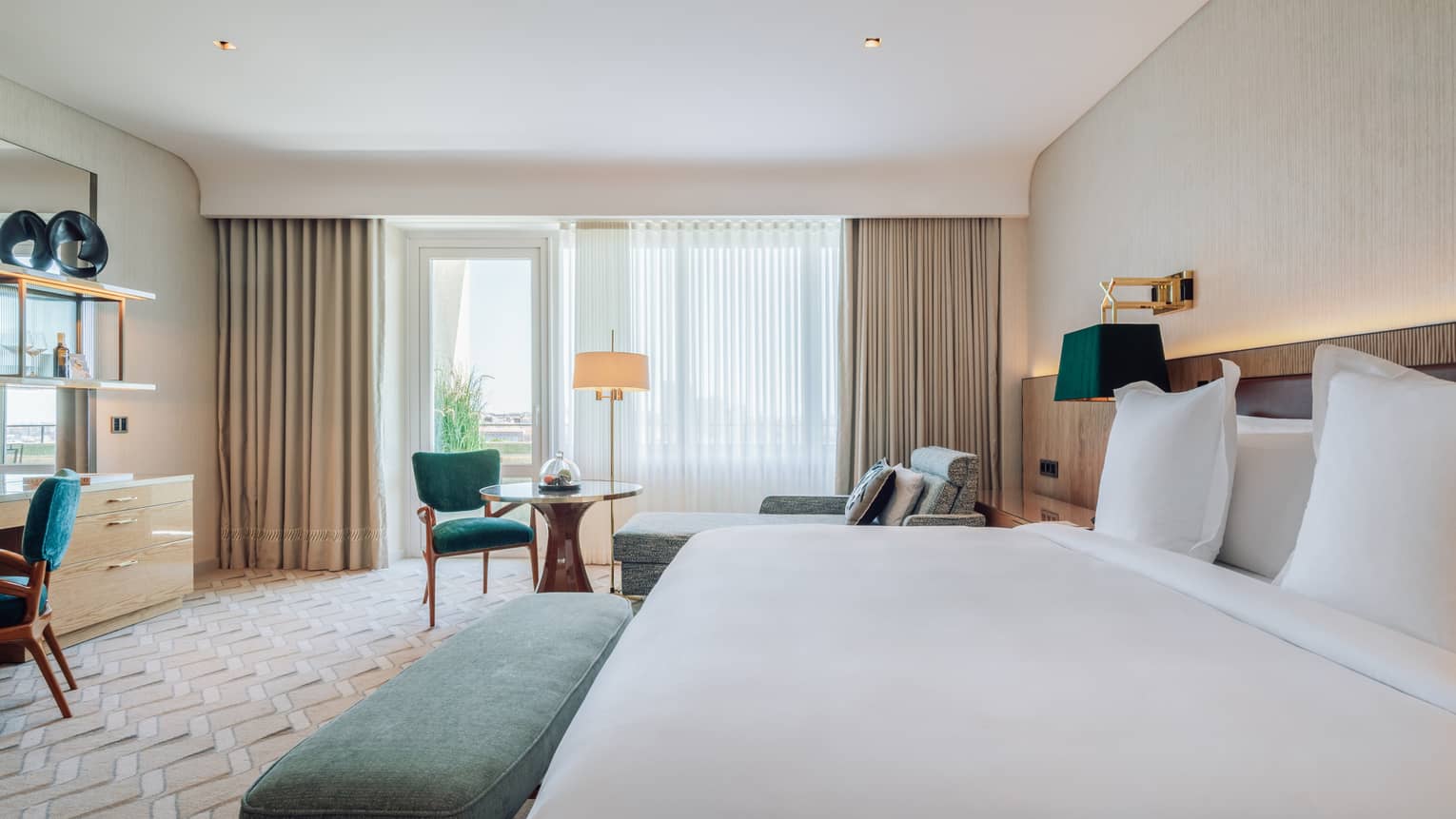 Hotel room with white king bed, turquoise bench, small round table and chair